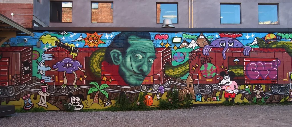 A Junction mural along a wall on Dundas Street West, a large green face among brightly coloured cartoon figures