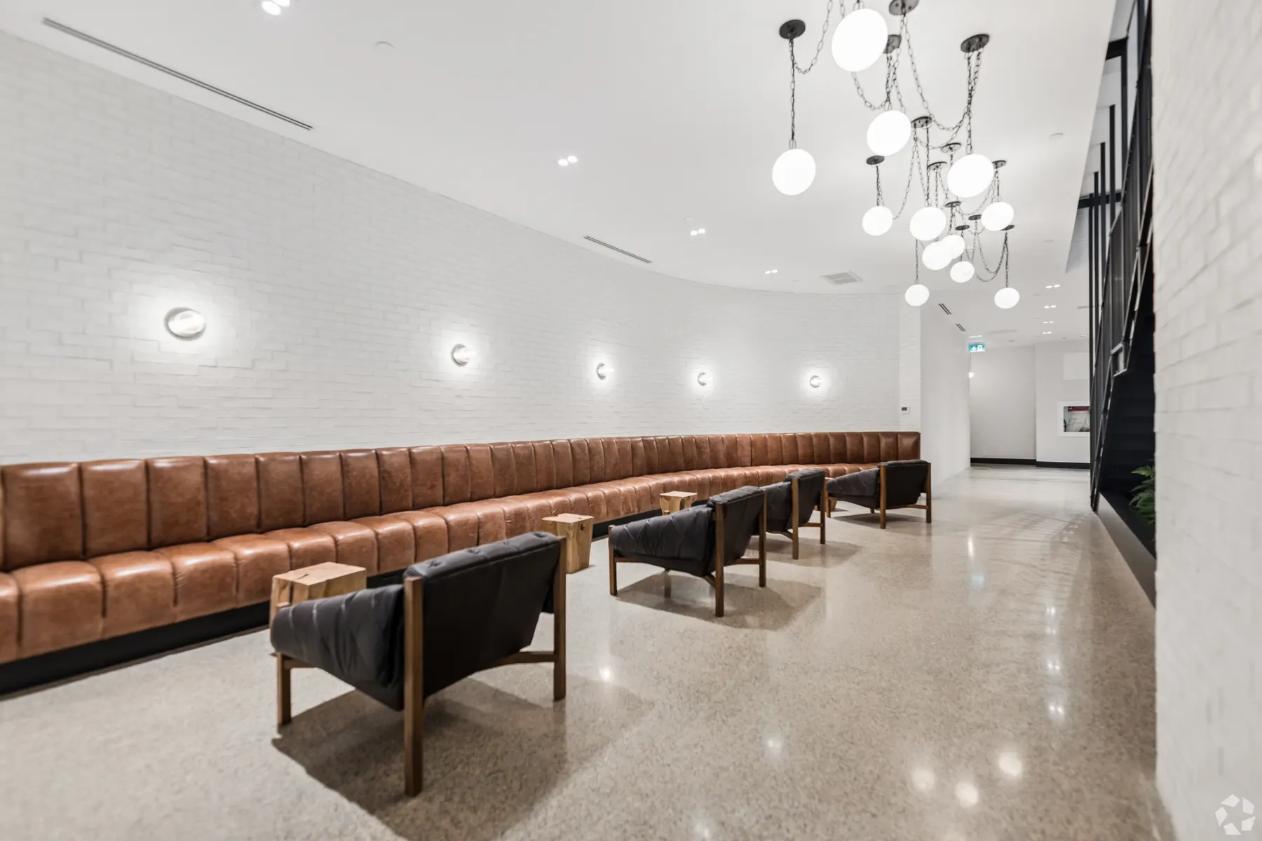 The lobby of The Pacific: a tan leather banquette running the length of a white brick wall lit by wall sconces, low black armchairs facing it across polished terrazzo, under a cluster of glass globe pendants