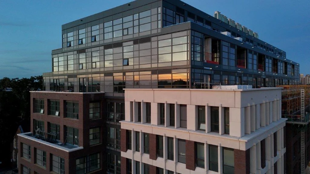 The upper floors and roofline of The Pacific from above at dusk, the stepped terraces and glazed top floor over the neighbouring rooftops