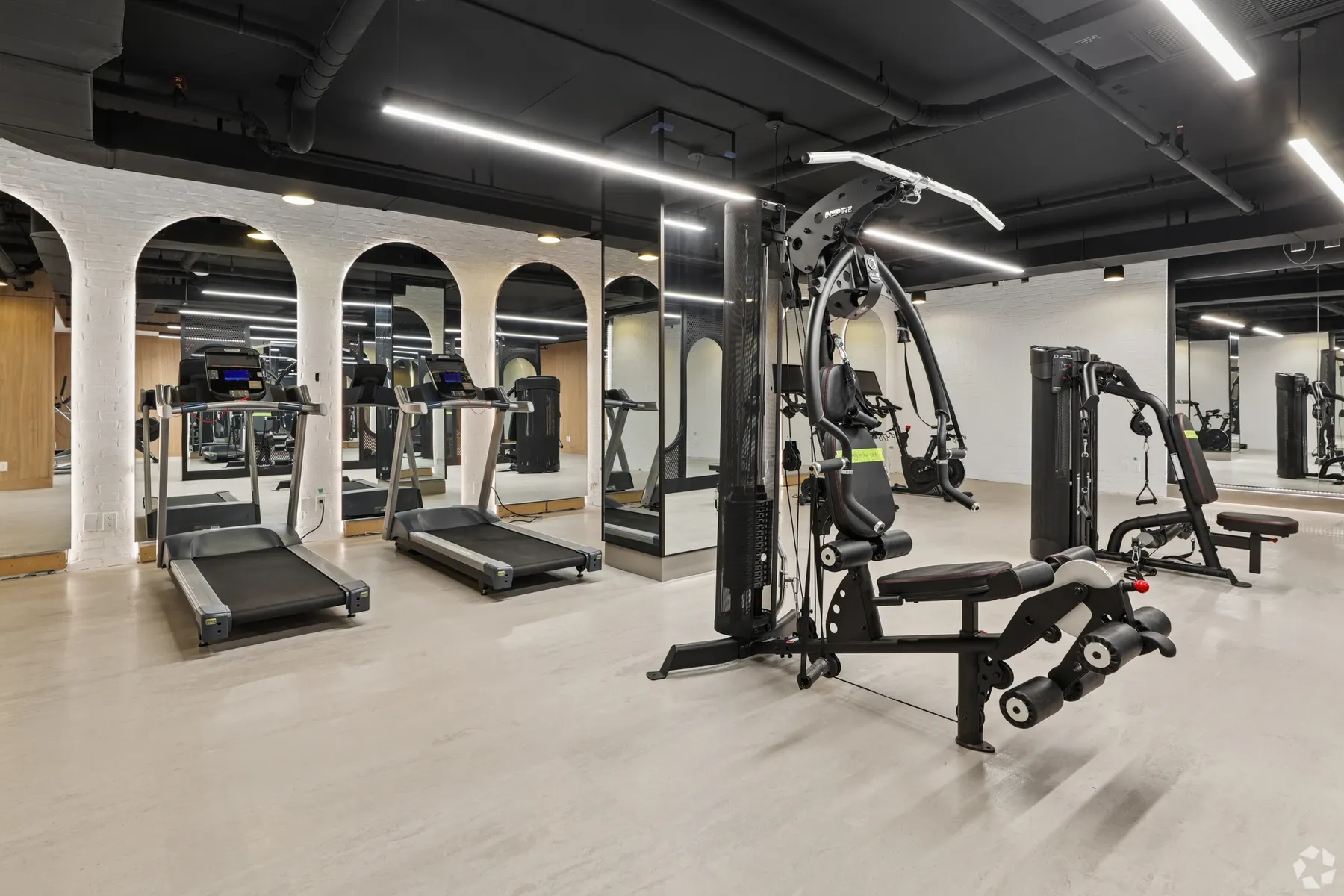 The fitness centre: treadmills and a cable weight machine on a pale floor, a bench and free weights beyond, under a black ceiling between arched wood alcoves