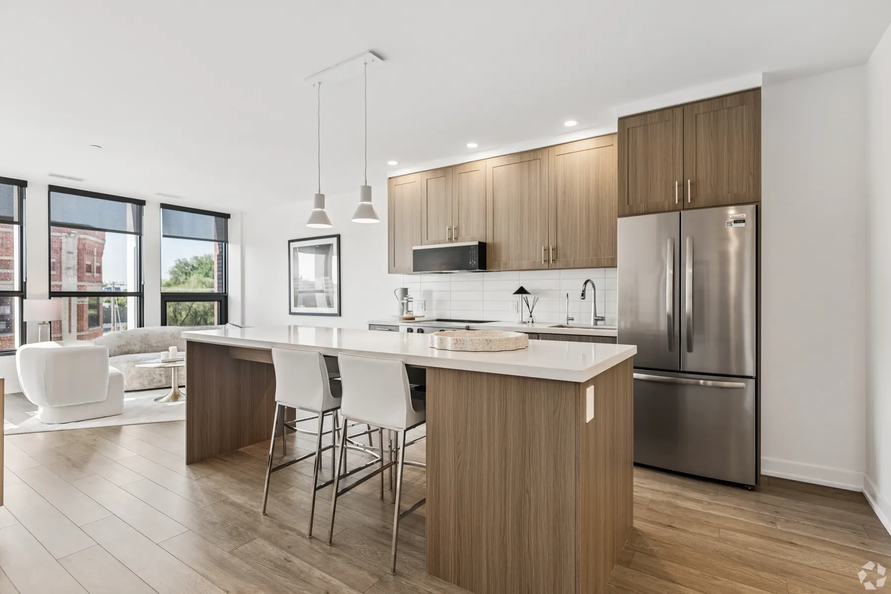 A two bedroom suite kitchen: walnut cabinetry and a stone island with three stools, the living room and its window wall beyond