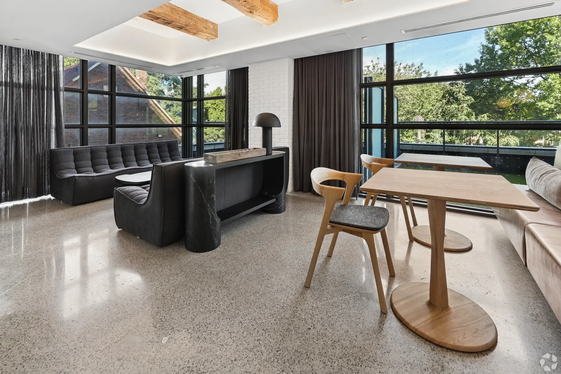 A resident lounge: a black leather banquette and a round oak table on polished terrazzo under a reclaimed timber beam