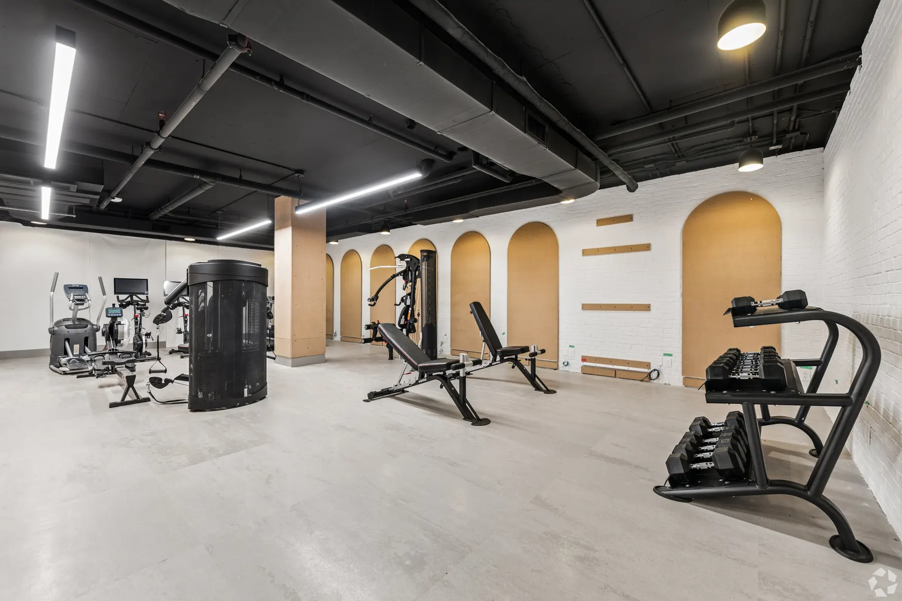 The fitness centre: cardio machines, a weight bench and racked dumbbells along a wall of arched wood alcoves, under a black ceiling