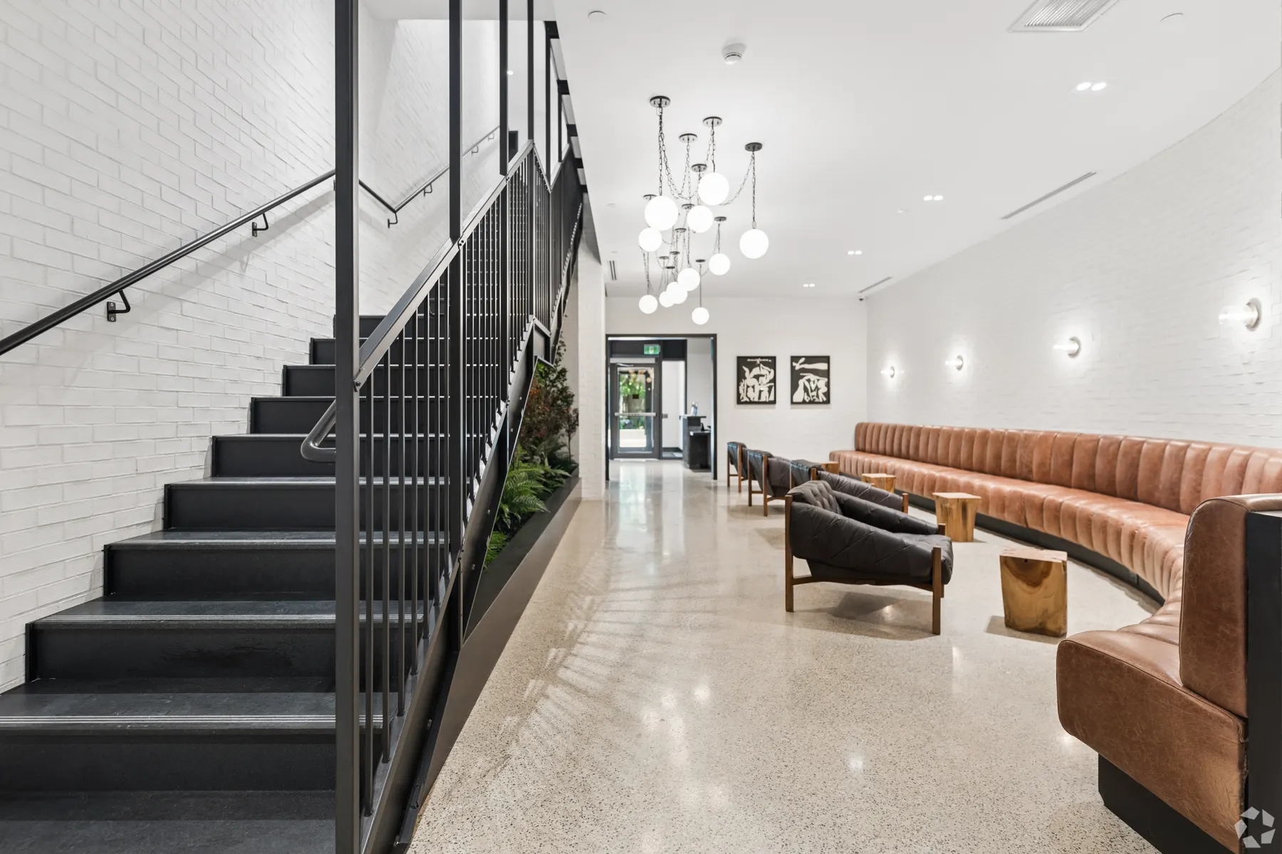 The lobby stair: a black steel staircase and railing against white brick, a planted bed alongside it, the banquette and the entrance beyond