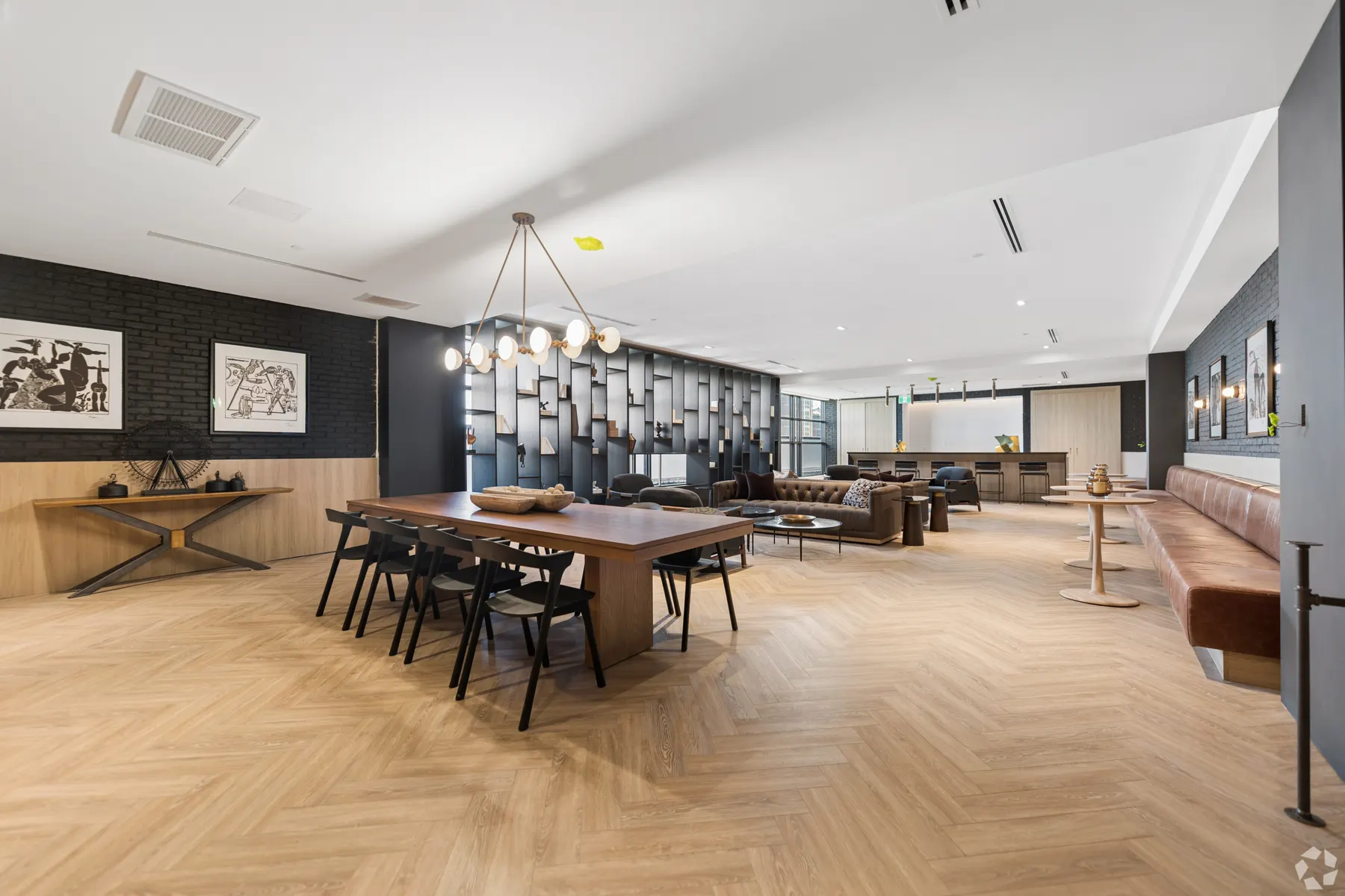 The party room: a long walnut table under a branched globe chandelier, seating and the bar beyond on herringbone floors