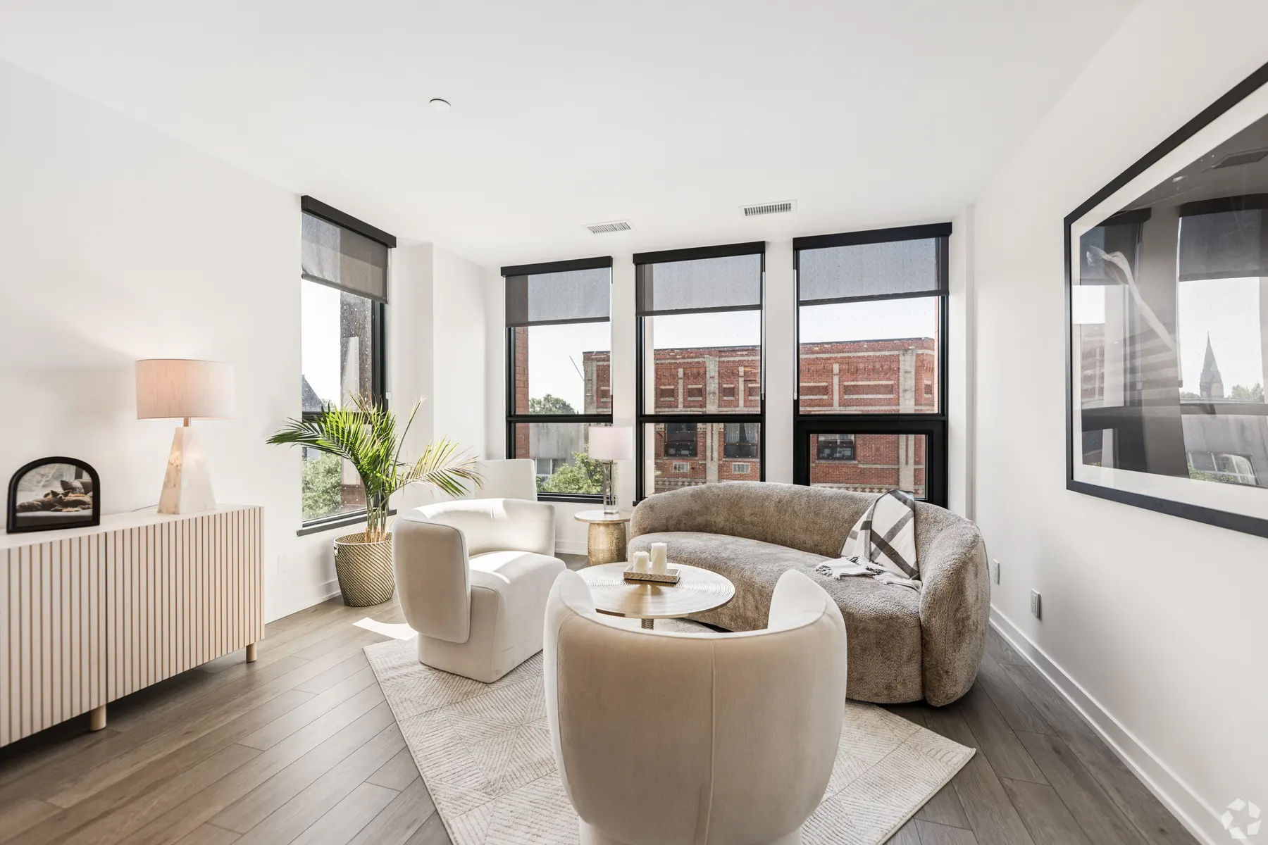 A two bedroom suite: a living room with bouclé seating around a round marble table, three window walls onto the brick rooftops of the Junction